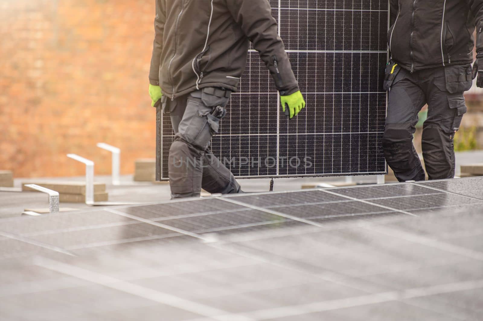 The process of installing solar panels. Solar panel installers work on the roof. Installers carry solar panel module to installation site, green and renewable energy concept.