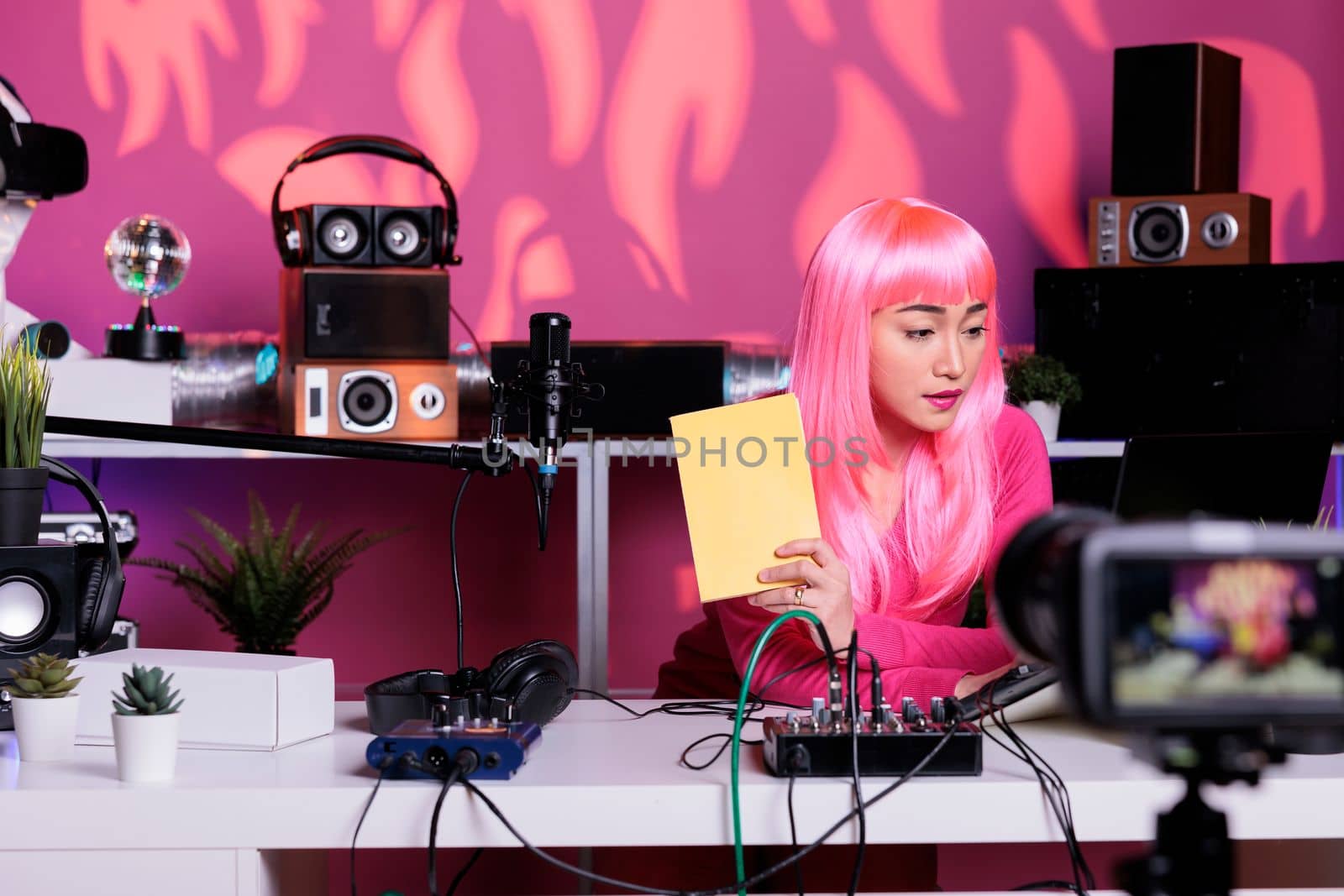 Asian vlogger sitting at desk table in streaming studio recording school supplies review showing notebook at camera., live streaming. Asian creator filming vlog posting content on her channel.