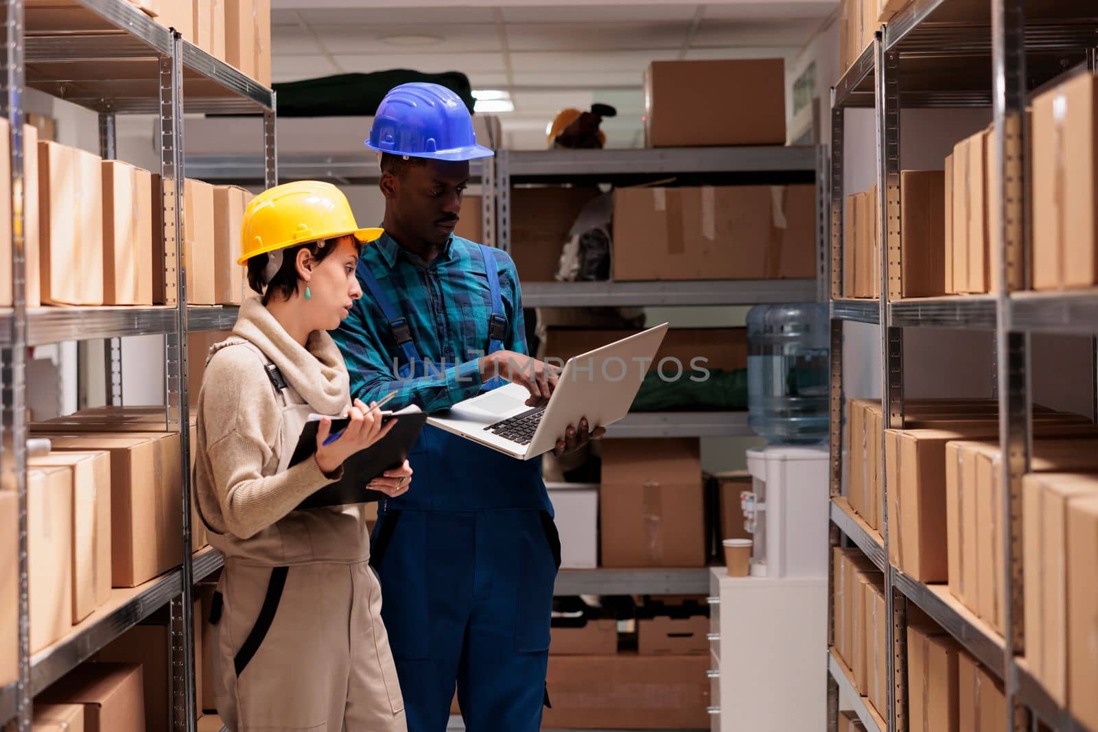 Warehouse supervisors discussing goods inventory and checking report on laptop. Man and woman diverse storehouse coworkers overseeing freight receiving and maintenance operations