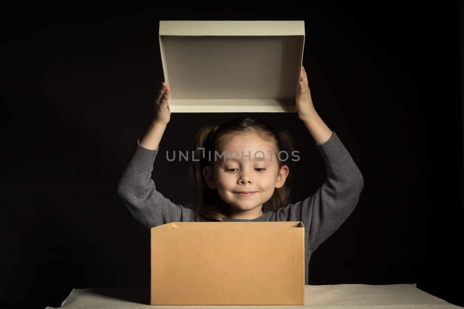 A little girl opens a long-awaited parcel with a gift, copy space on cardboard box.
