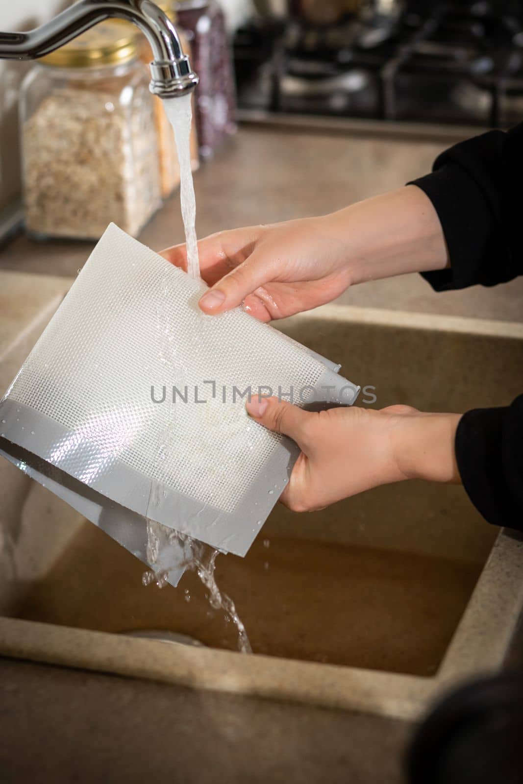 Silicone baking mat is washed under an open stream of water after cooking in the kitchen.