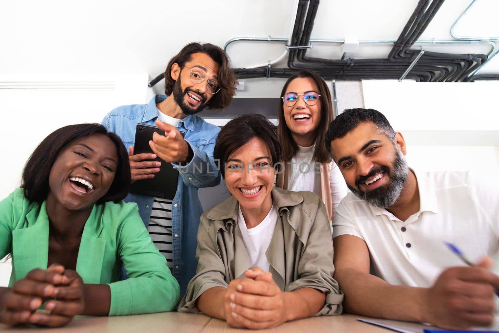 Screen view of group of multiracial coworkers looking at camera and lauging during video call in the office. Business and technology concept.