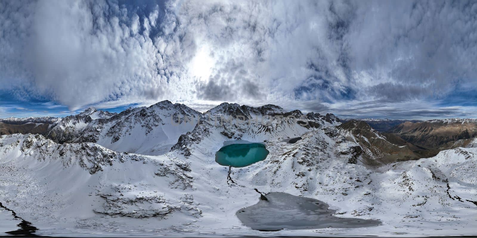 panorama of mountain snow-covered range with turquoise lake, sunny day with clouds.