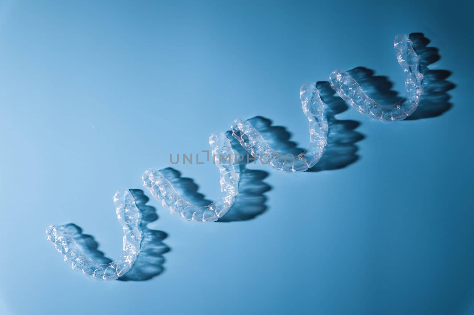 background for dental clinic or orthodontics. invisible plastic new braces lie in a row on a blue background, studio shot with shadows.