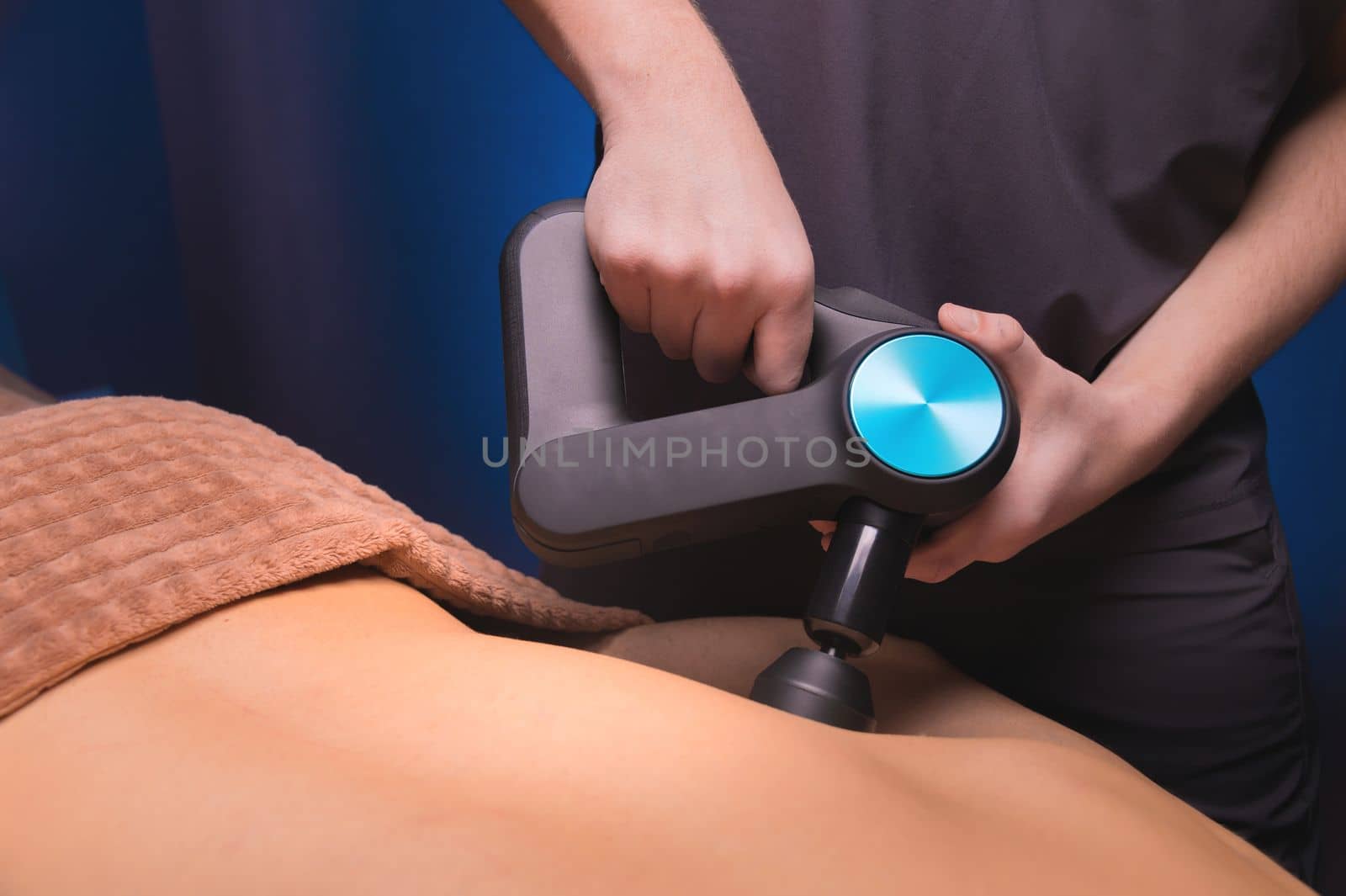 Percussive massager, sports man getting his back massaged to relieve pain, top side view close-up.