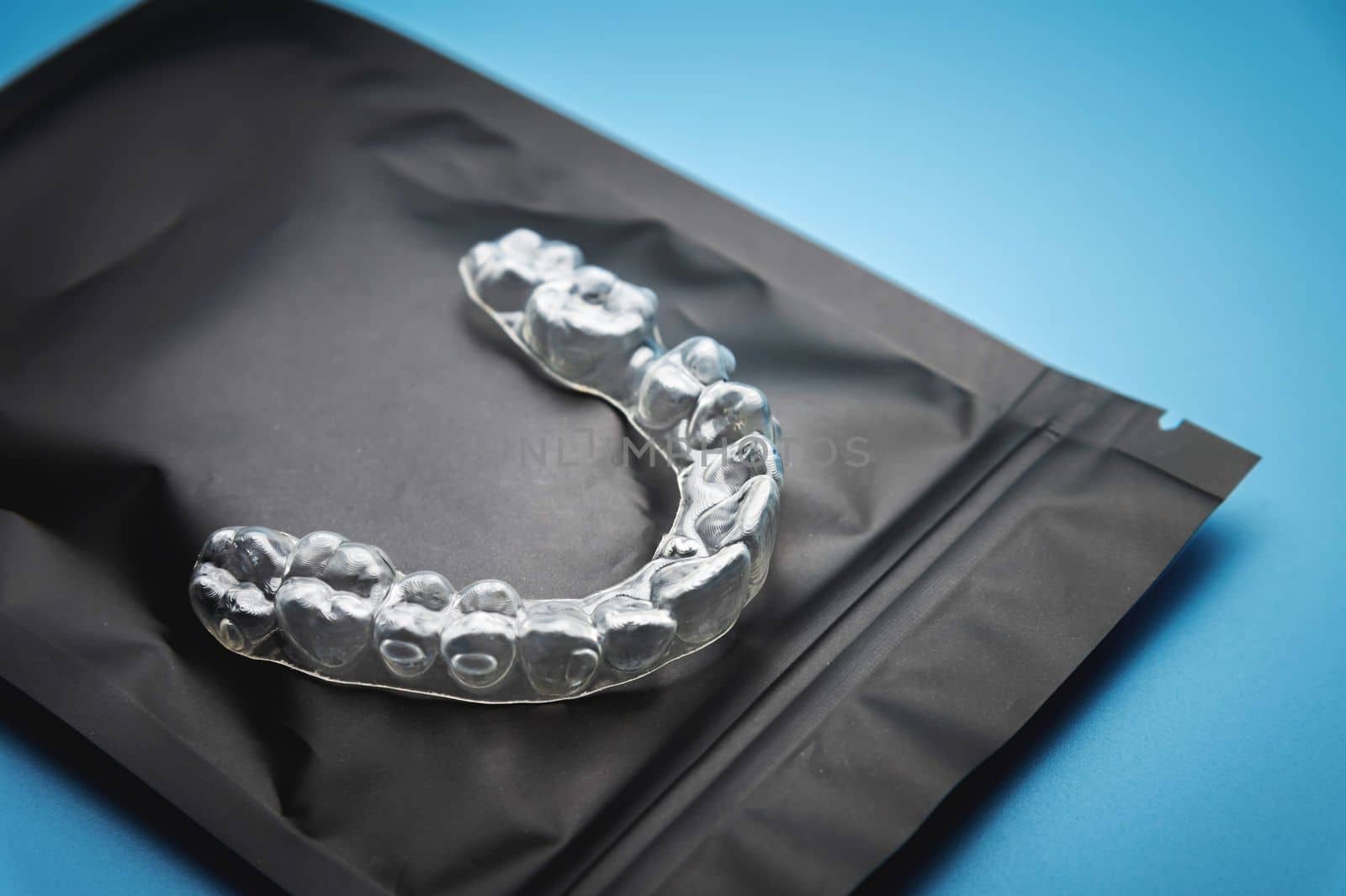 close-up, invisible plastic braces on a black special zip package, lying on a blue background. studio shot, dental clinic background by yanik88