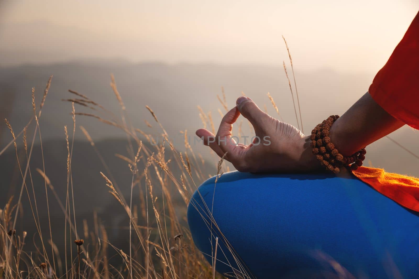 close-up of elegant female hands with rosary holding fingers, lotus position in the grass in the mountains at sunset.