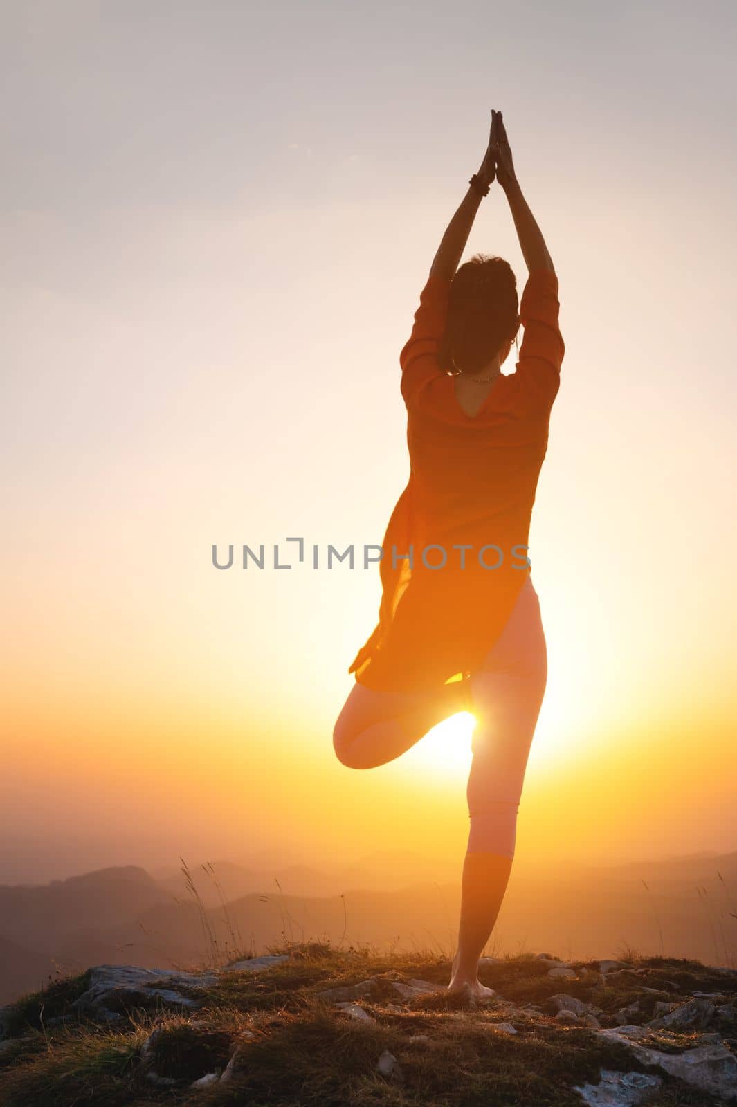 a woman stands in a yoga pose against the sun in the mountains, a silhouette of a sporty woman.
