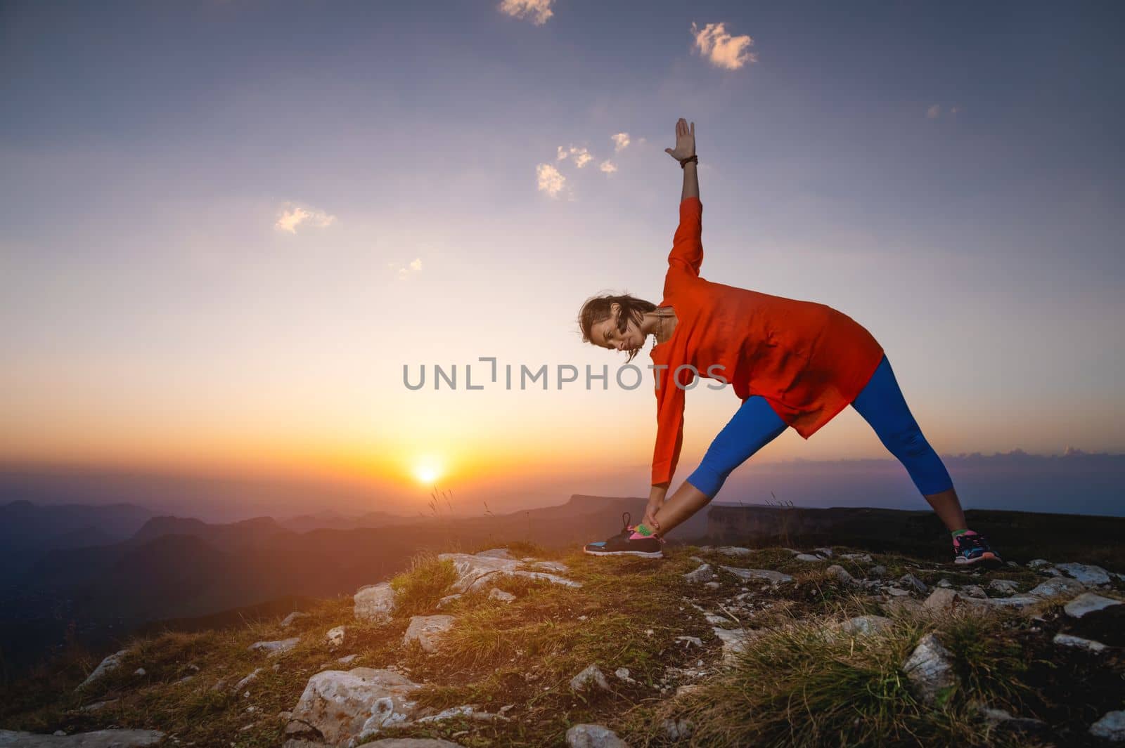 woman in warrior pose in mountains, yoga practice outdoors at sunset.