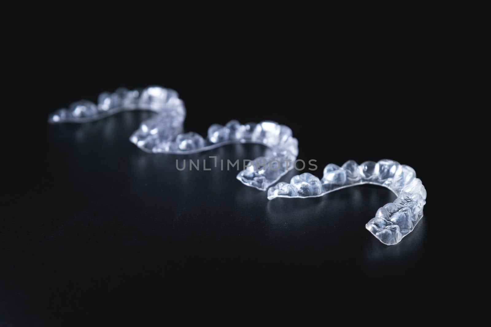 three invisible plastic aligners lie next to each other on a black background by yanik88