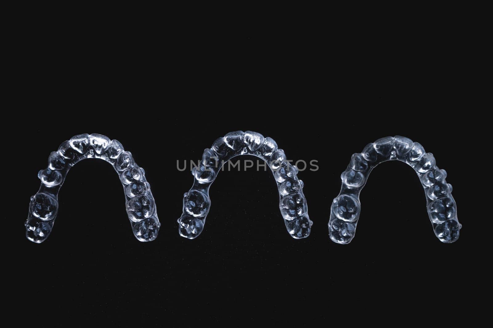 three invisible plastic aligners lie next to each other on a black background by yanik88