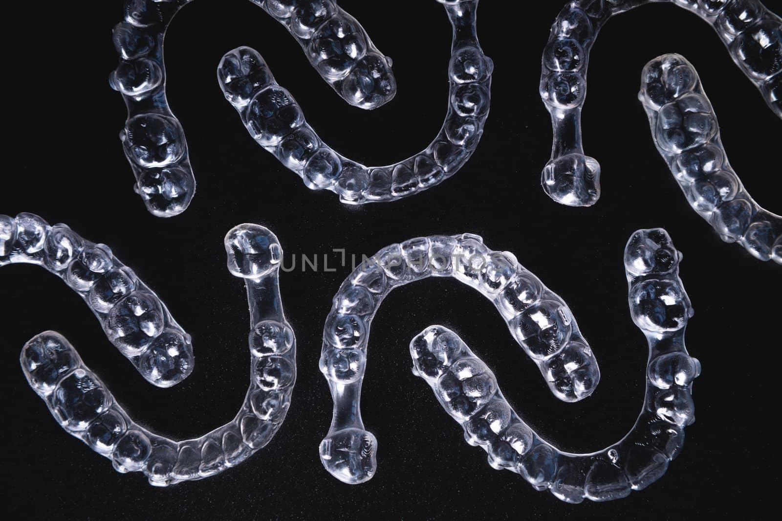 a pattern of invisible plastic aligners lie on a black background.