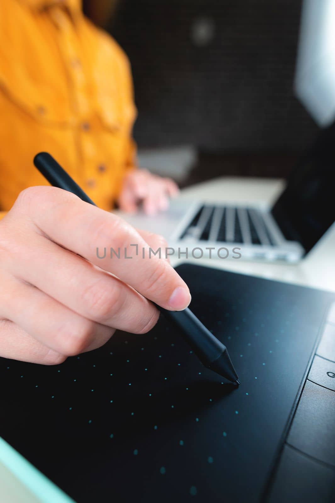 Casual man, freelancer with stylus, writing on digital tablet screen, working on laptop computer at office desk. Graphic or web designer working on his web design project, close up.