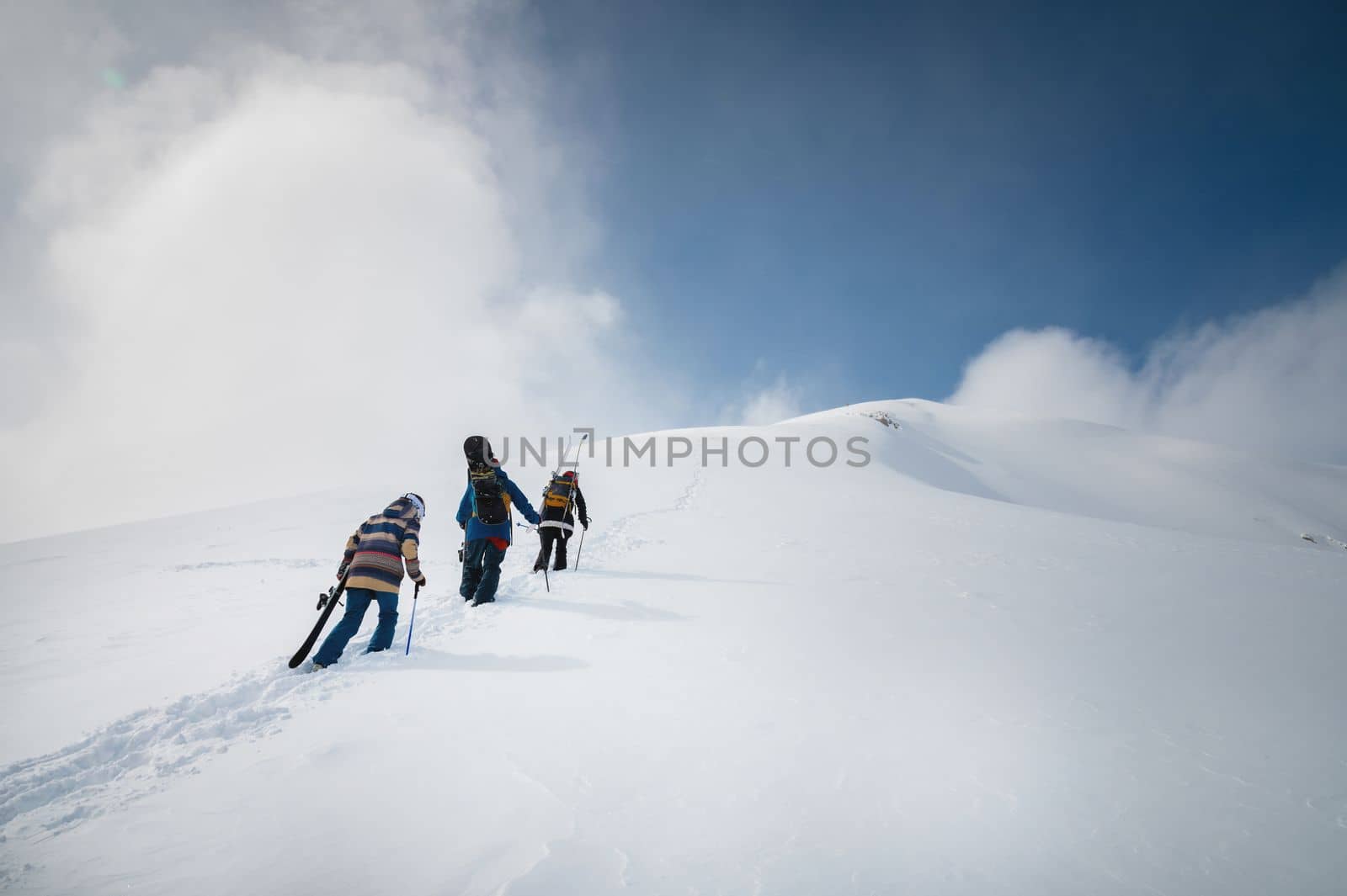 snowboarder and skier go uphill carrying equipment. off-piste skiing, freeride on a sunny day.