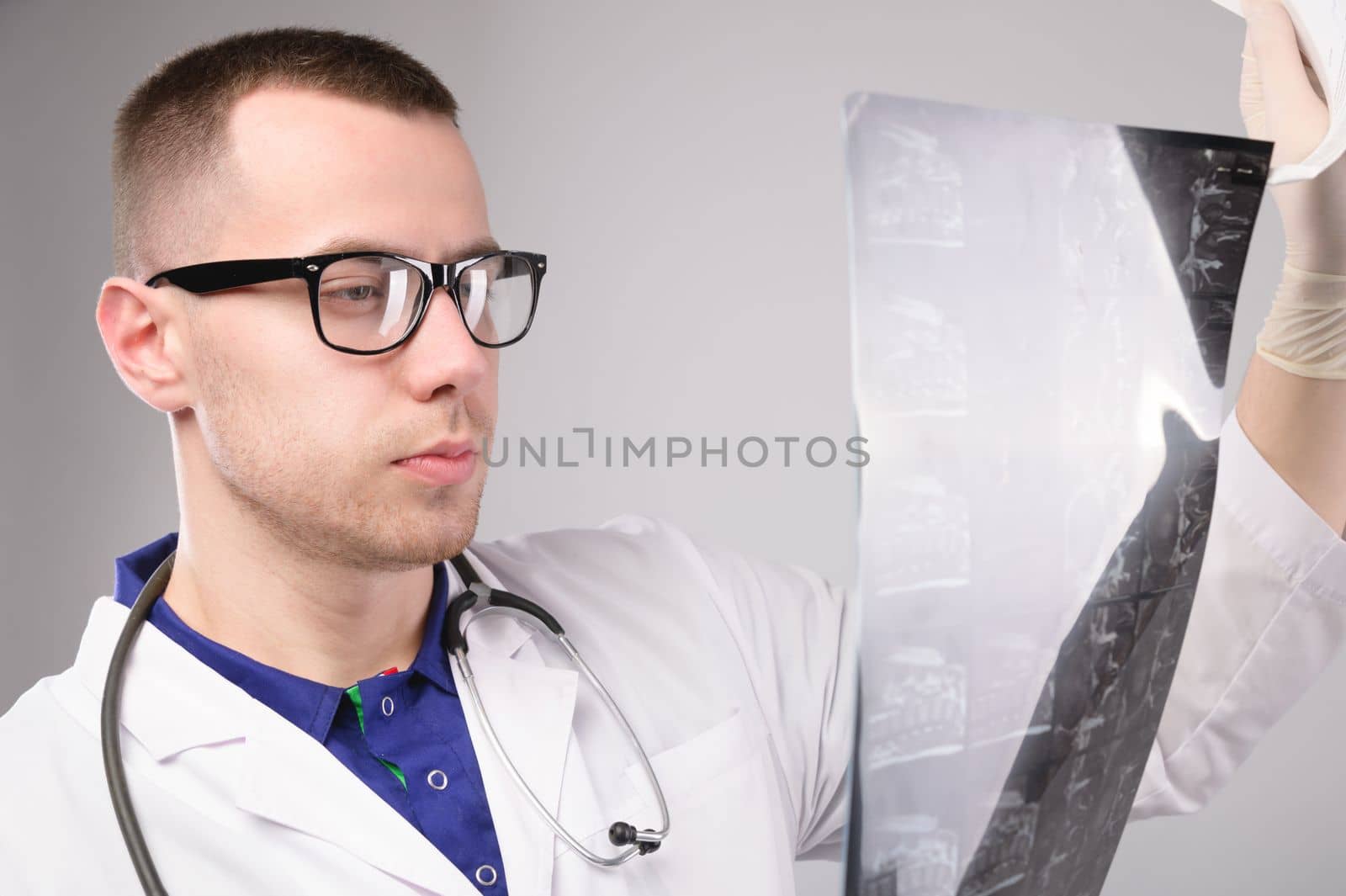 Young male doctor looking at an x-ray in a hospital on a white background, portrait of a specialist in uniform by yanik88