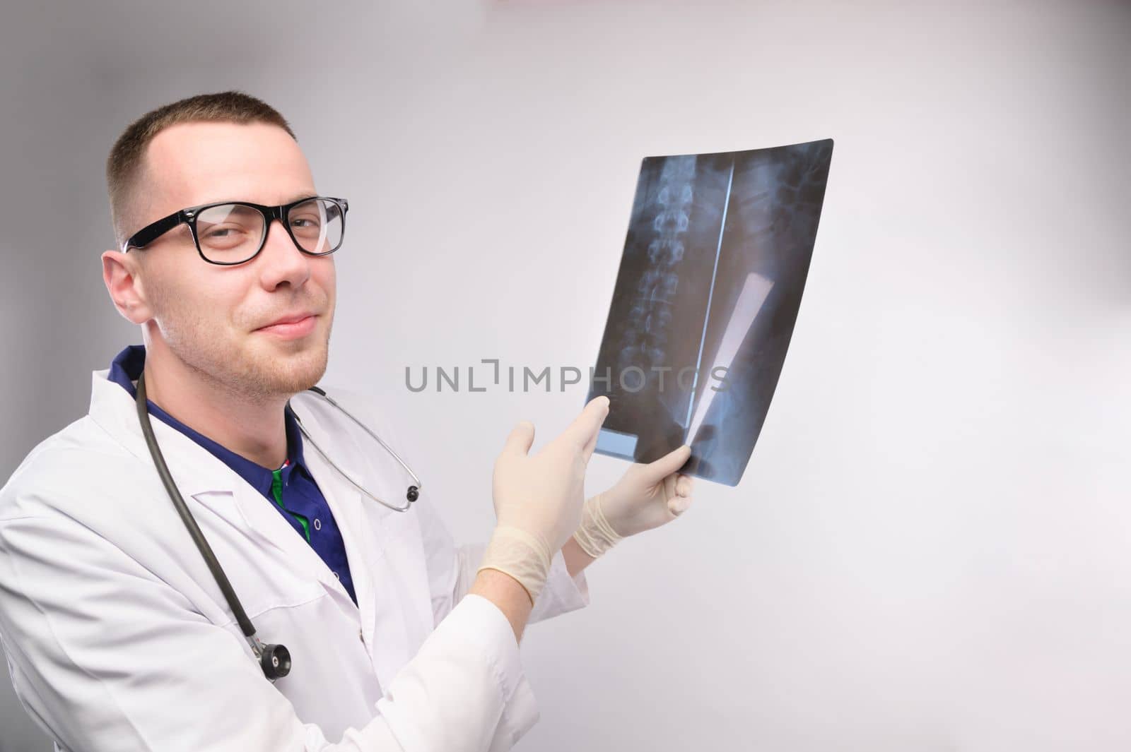 doctor young man in glasses looks at the camera and smiles showing x-rays of the human spine. studio portrait.