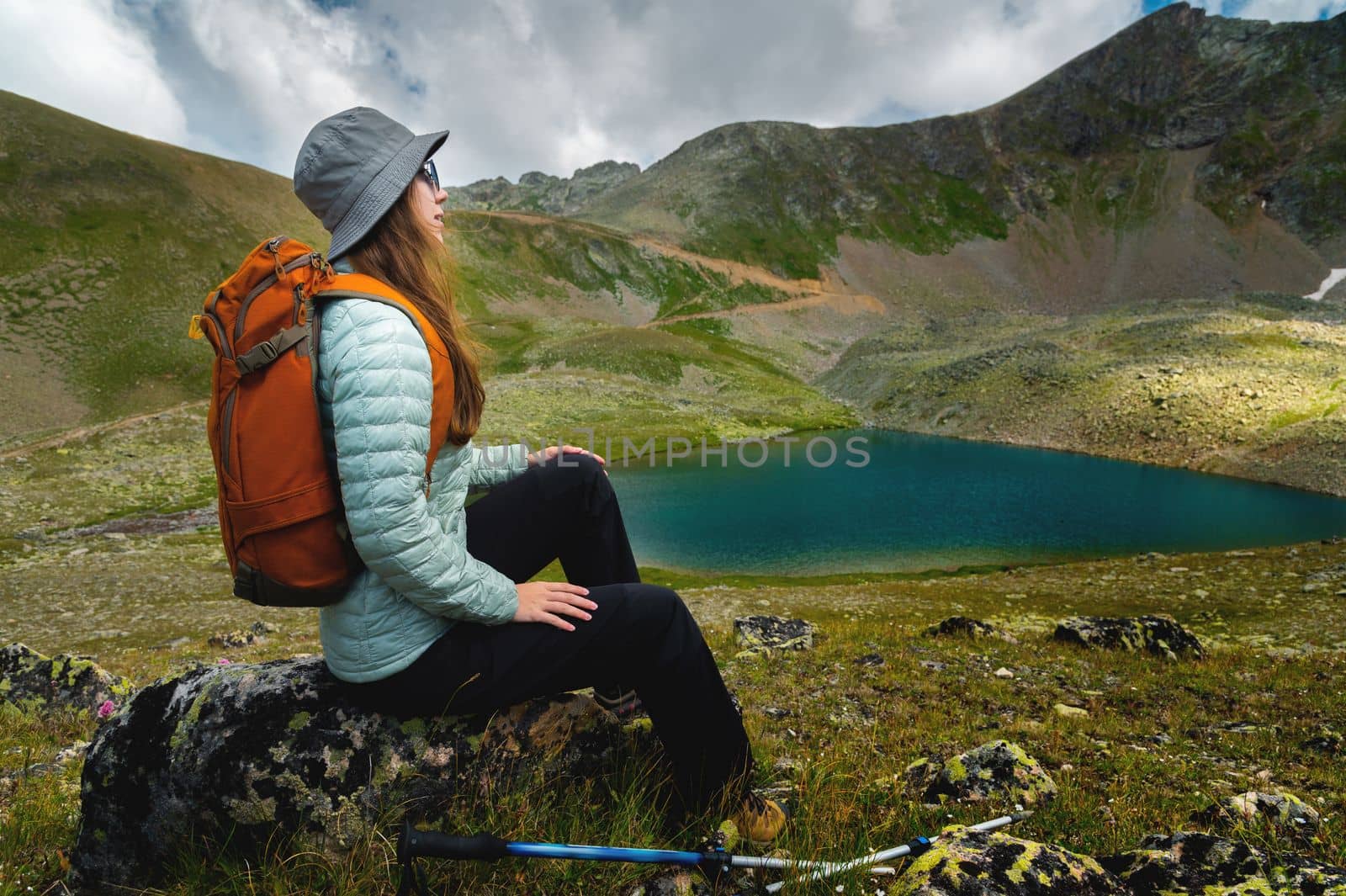 a woman tourist sits with a backpack with her back to the camera near a mountain lake. hiking vacation.