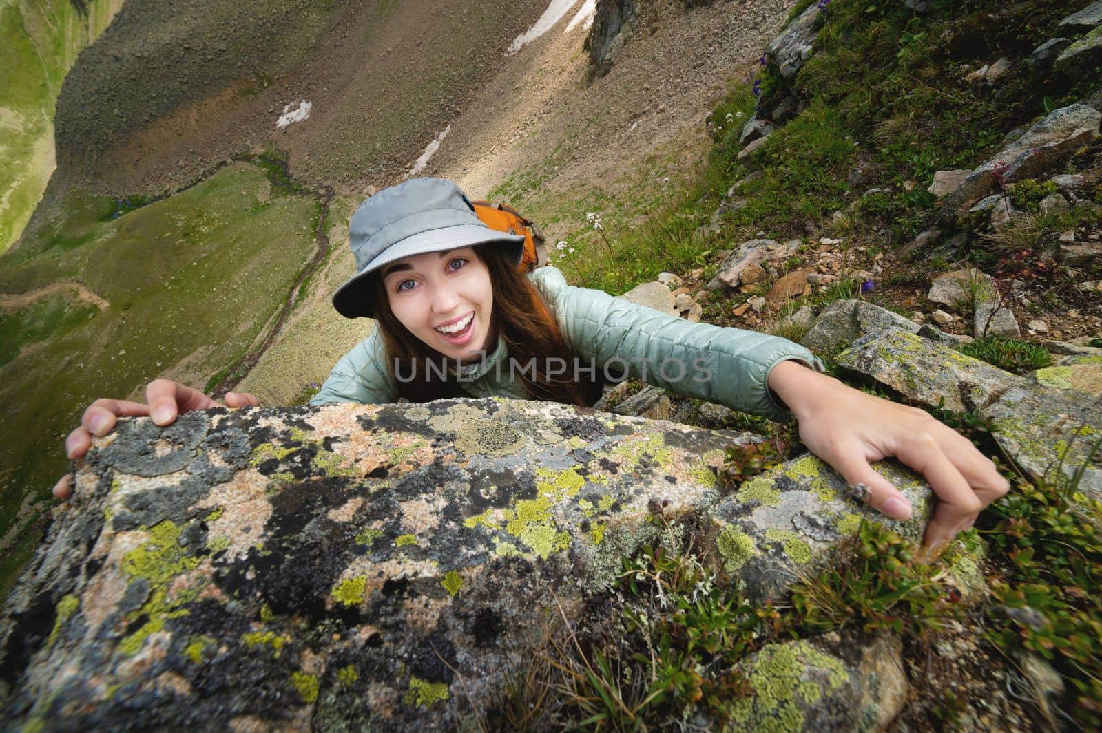 happy woman climbs a rock while trekking outdoors. carefree backpacker smiling at camera.