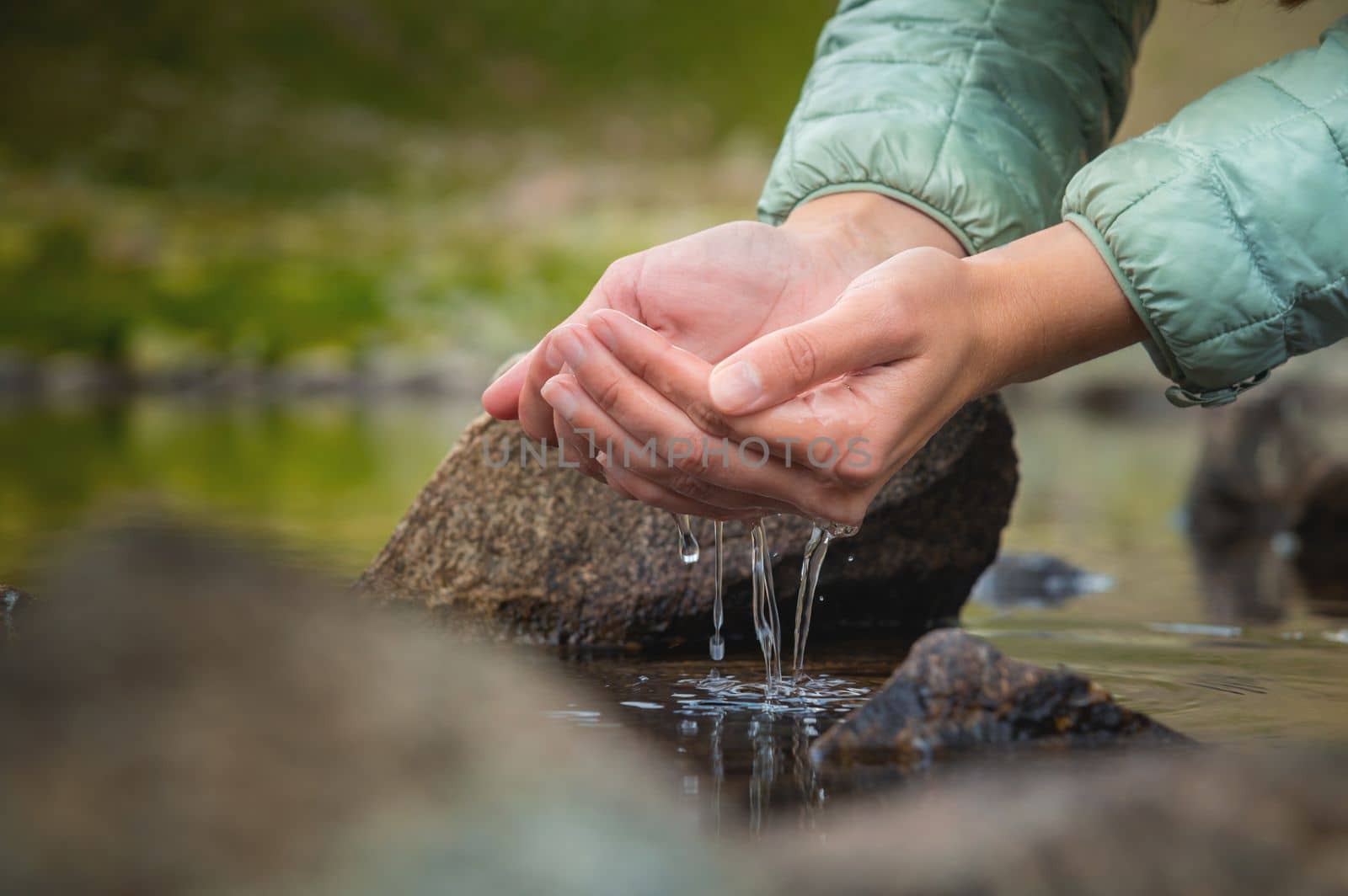 Close-up of water drops falling from female hands into a stream. The hand touches fresh water. A tourist drinks water from a reservoir in the mountains in summer on a sunny day.