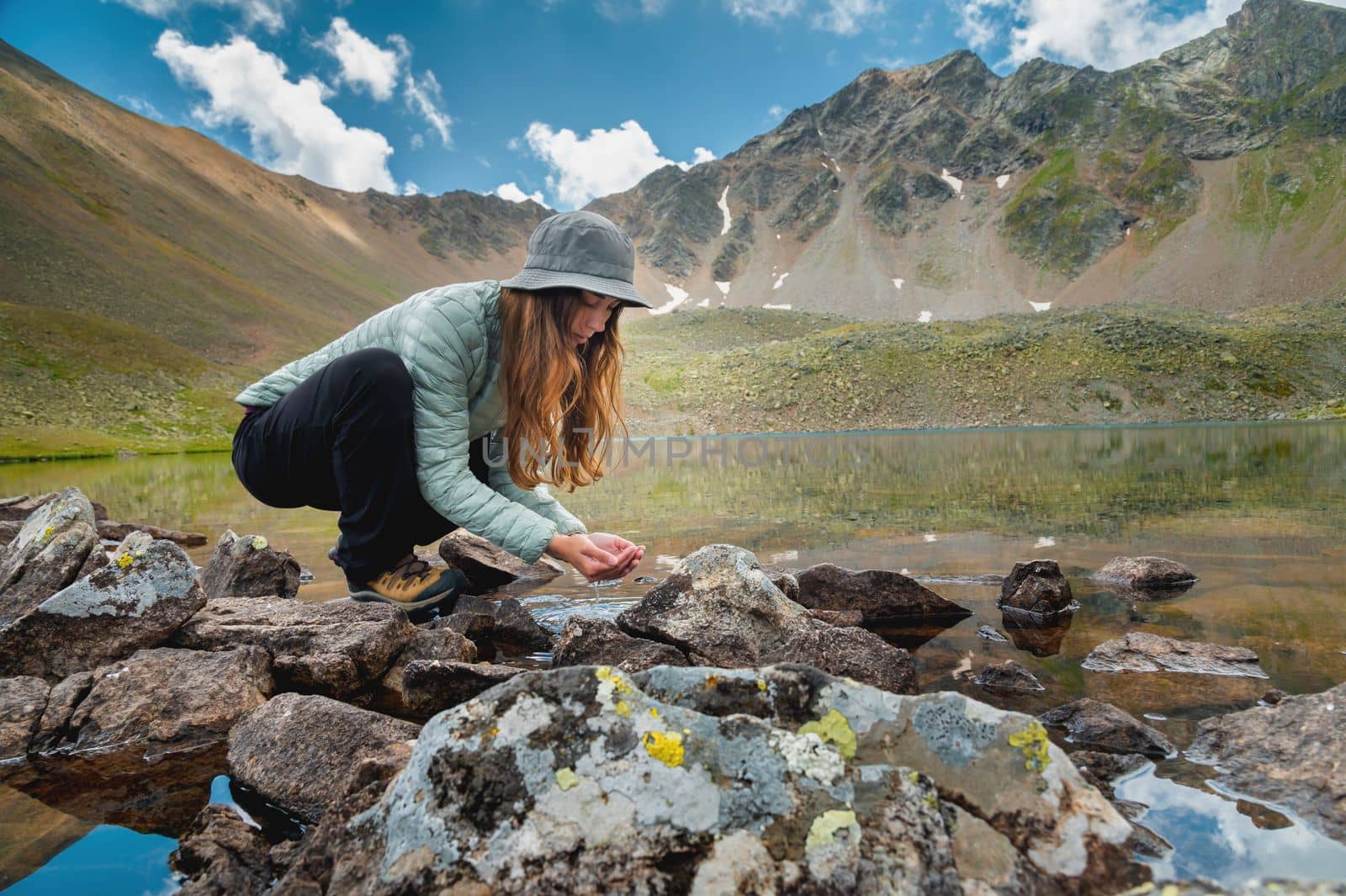 A young girl fills her hands with water from a stream of a cold mountain lake in order to drink and refresh herself. Happy hiker on a hike.