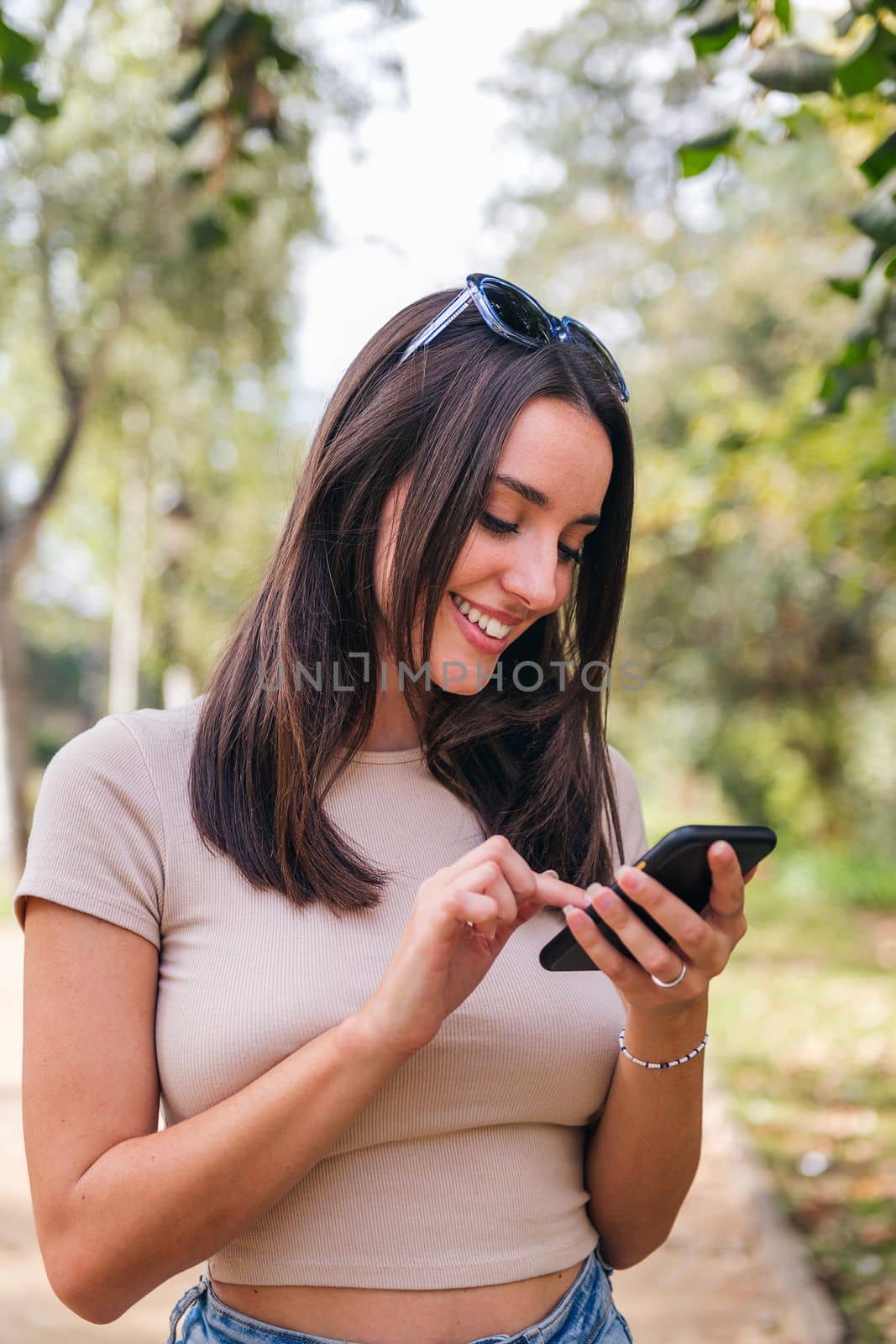 smiling young caucasian woman using her mobile phone in a park, concept of youth and technology of communication