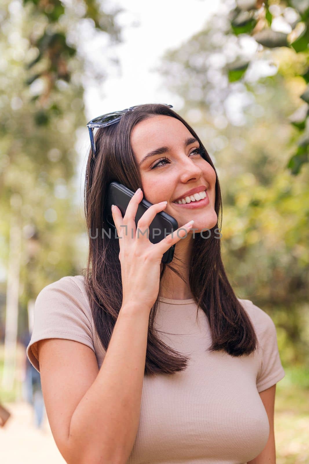 smiling young caucasian woman making a call with her mobile phone in a park, concept of youth and technology of communication