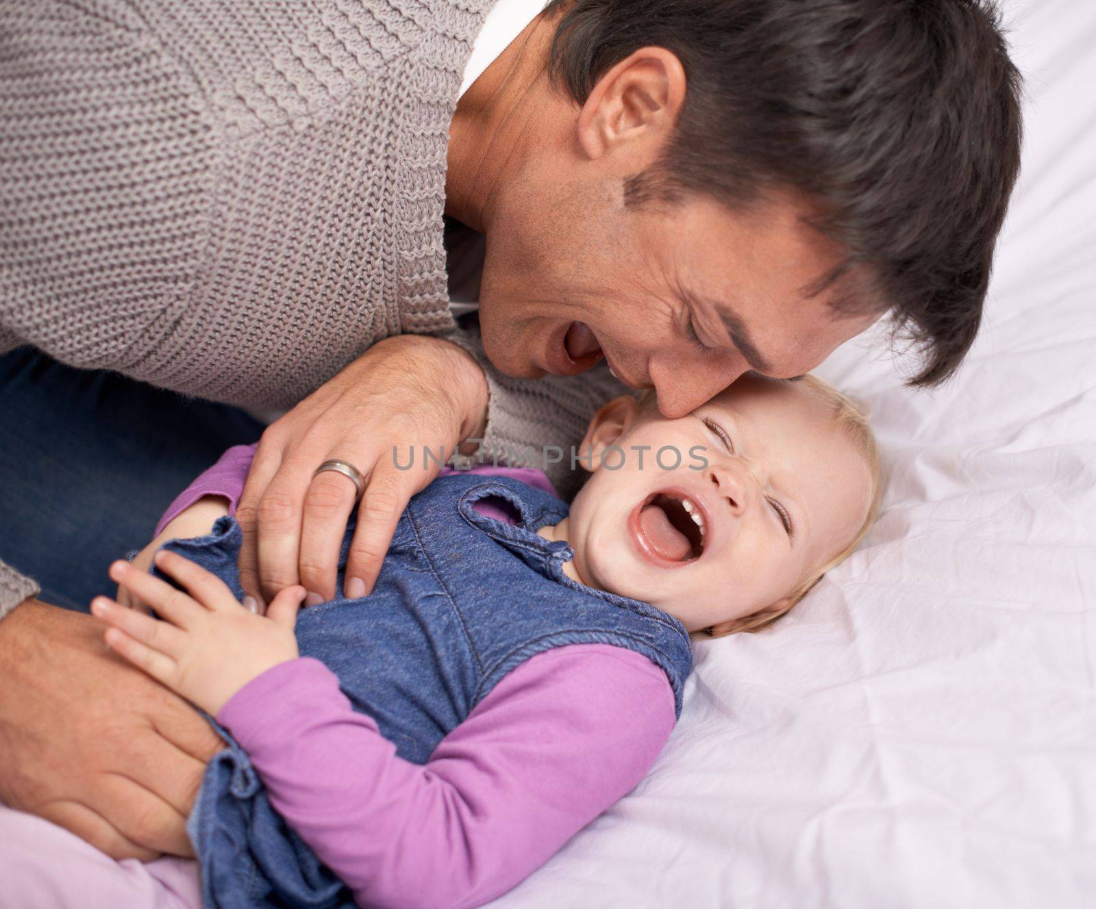 Im the tickle monster. A young father playing with his baby girl on the bed