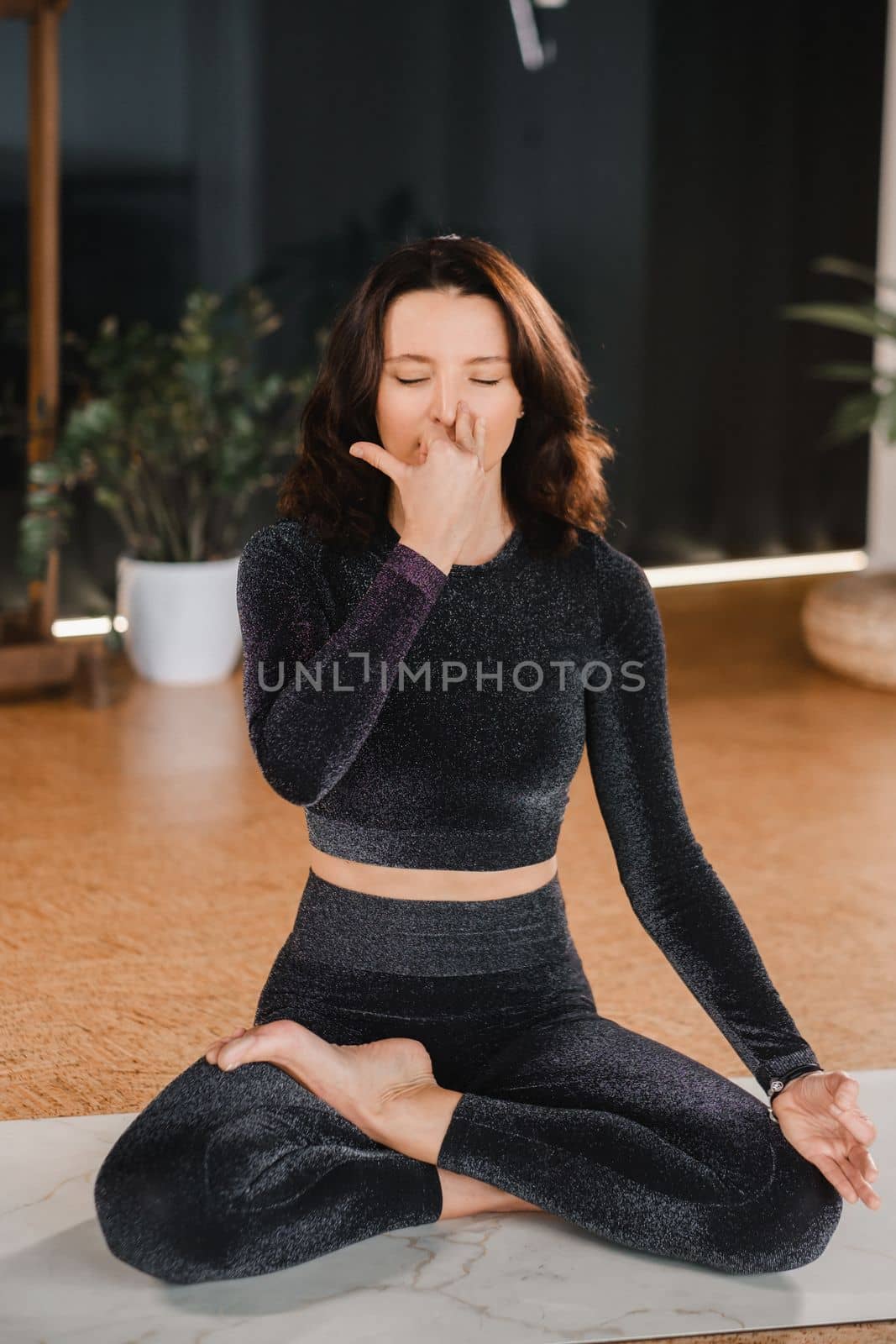 A woman in a black tracksuit sits on a yoga mat in a lotus position in the gym.