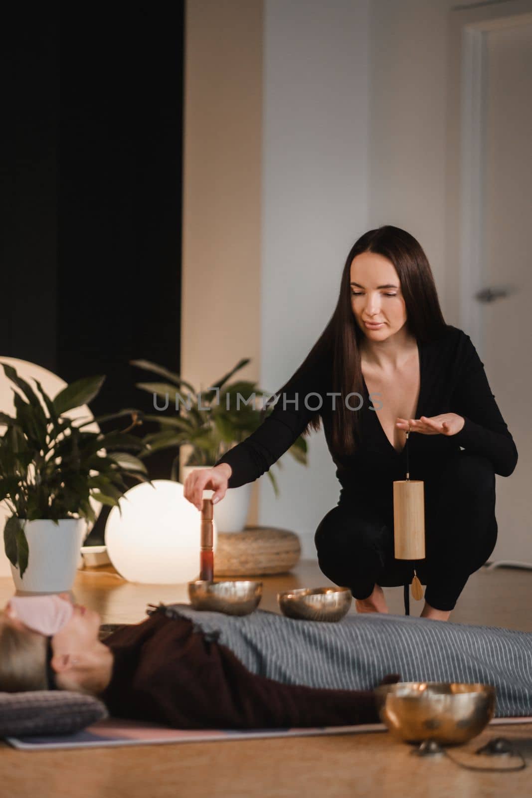 A young beautiful woman is doing a massage with singing bowls and a koshi bell to another girl. Sound therapy by Lobachad