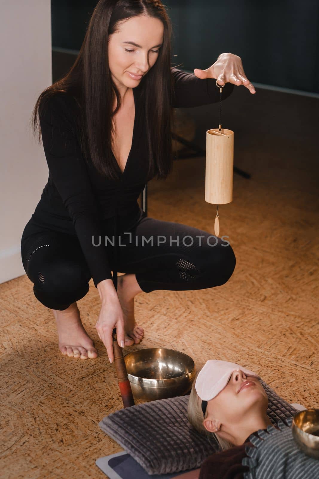 A young beautiful woman is doing a massage with singing bowls and a koshi bell to another girl. Sound therapy by Lobachad