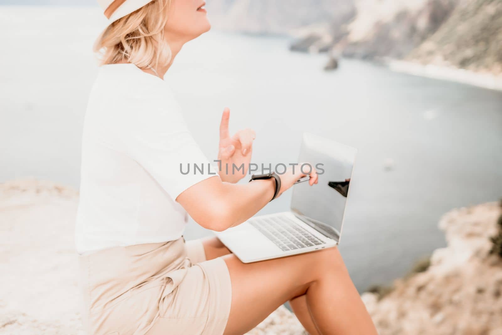 Digital nomad, Business woman working on laptop by the sea. Pretty lady typing on computer by the sea at sunset, makes a business transaction online from a distance. Freelance remote work on vacation