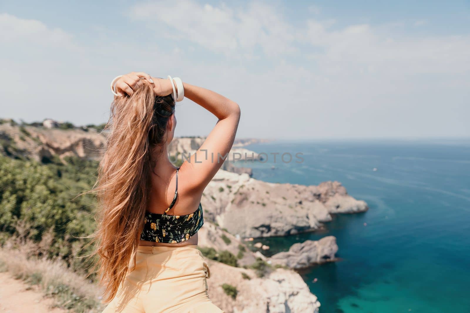 Woman travel sea. Happy tourist taking picture outdoors for memories. Woman traveler looks at the edge of the cliff on the sea bay of mountains, sharing travel adventure journey.