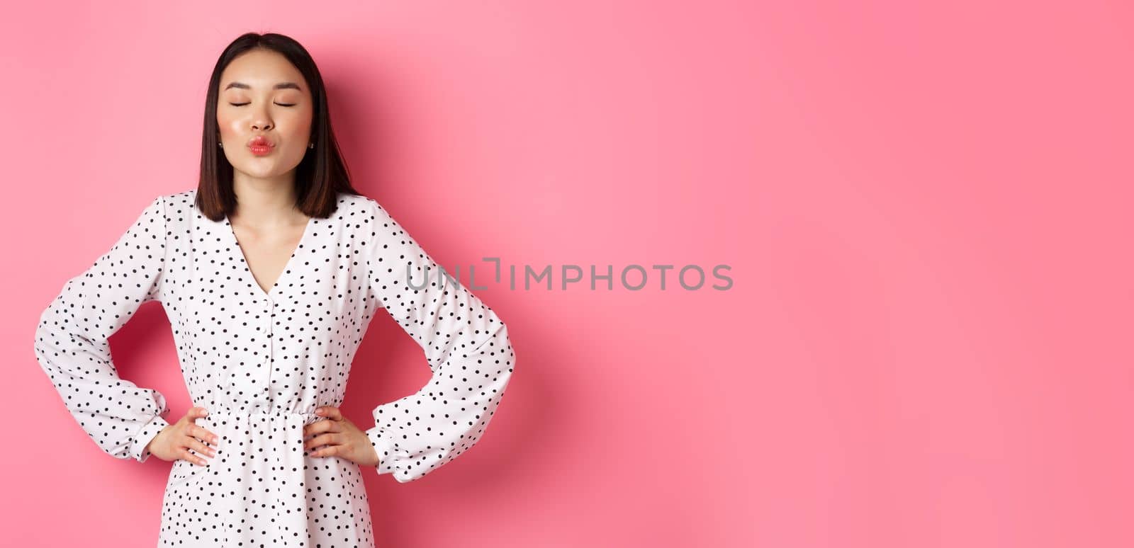 Beautiful asian woman in dress pucker lips and close eyes, waiting for kiss, standing over pink background by Benzoix