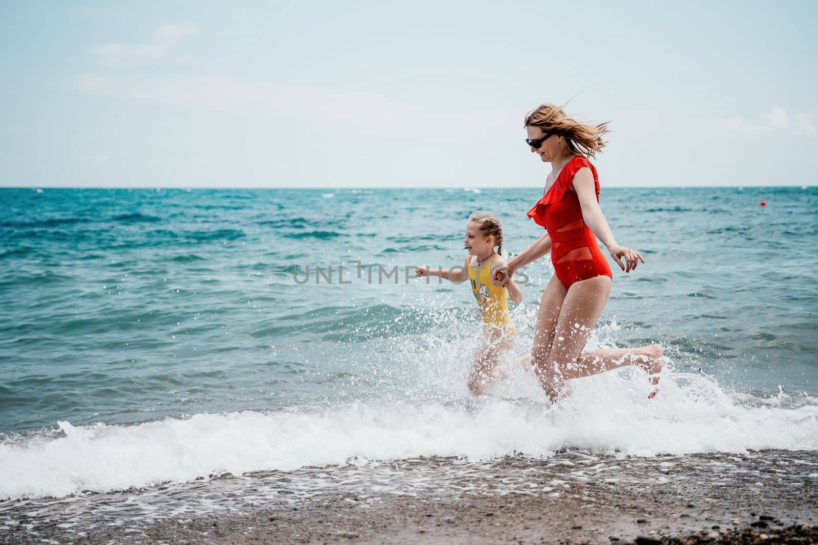 Happy loving family mother and daughter having fun together on the beach. Mum playing with her kid in holiday vacation next to the ocean - Family lifestyle and love concept.