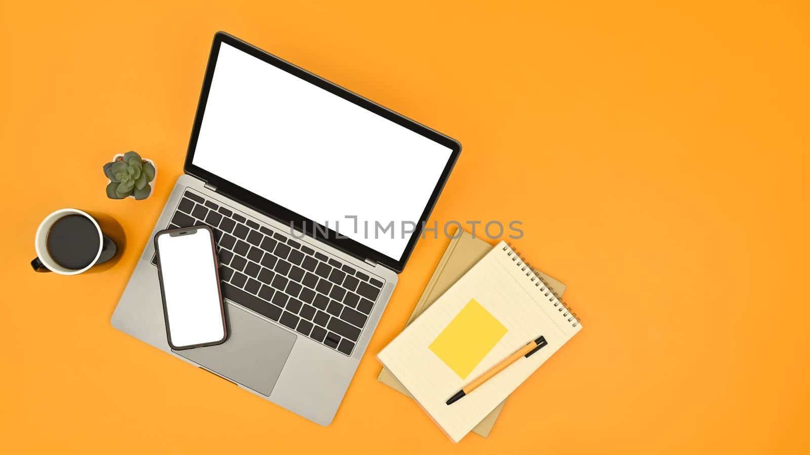 Laptop computer, mobile phone, notebooks, cup of coffee and succulent plant on yellow background.