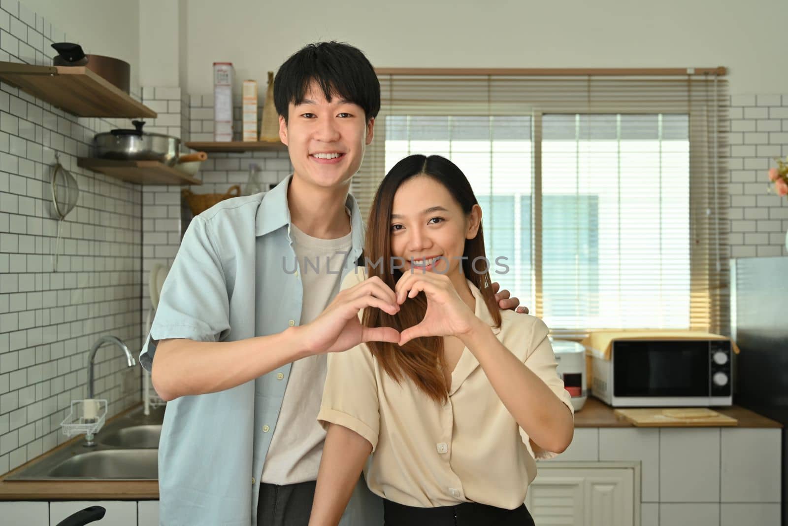 Portrait of beautiful young married couple making heart shape with their hands and smiling to camera.