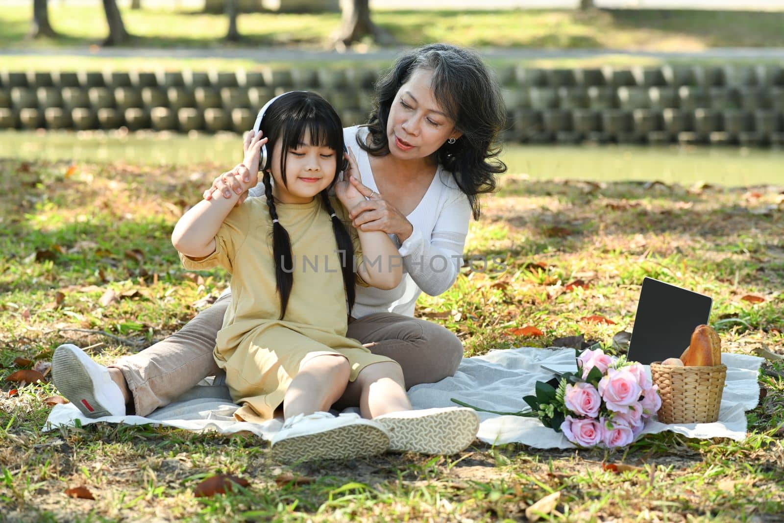 Adorable little grandchild listening to music in headphone while spending time outdoor mature grandmother by prathanchorruangsak