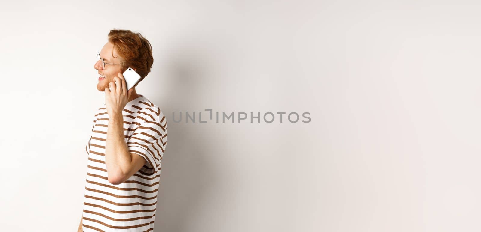 Profile of happy young handsome man talking on mobile phone, looking left and smiling, standing over white background by Benzoix