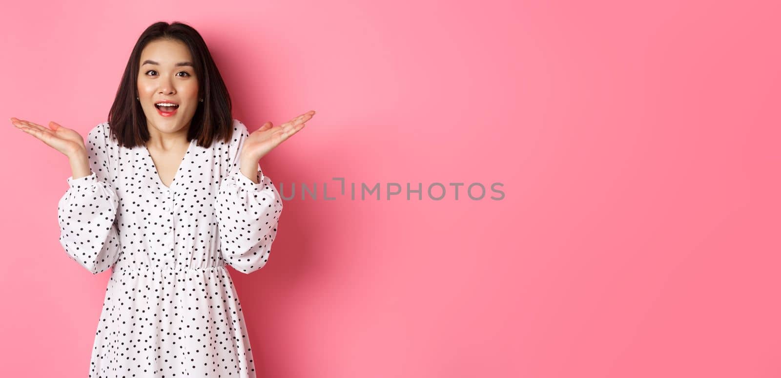 Image of surprised korean girl in dress, female model staring at camera and gasping amazd, standing over pink background by Benzoix