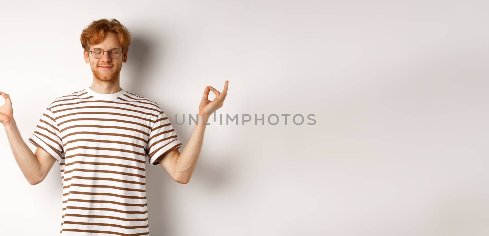 Calm and relaxed young man with red messy hair, spread hands sideways in mudra gesture and smiling, practice yoga or meditating, white background by Benzoix