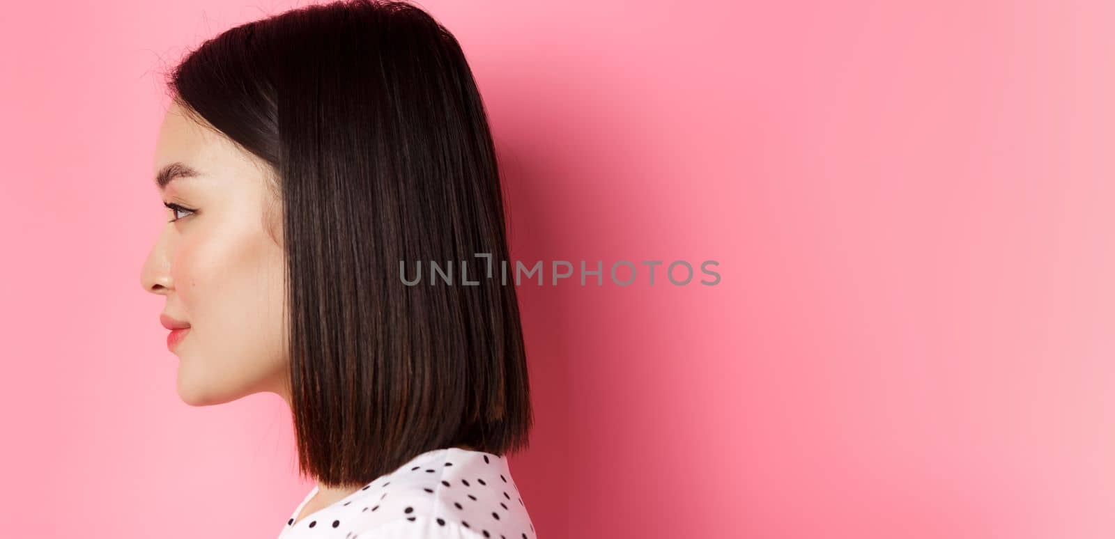 Beauty and skin care concept. Headshot profile of young beautiful asian woman with short dark hair, looking left at copy space, standing over pink background.