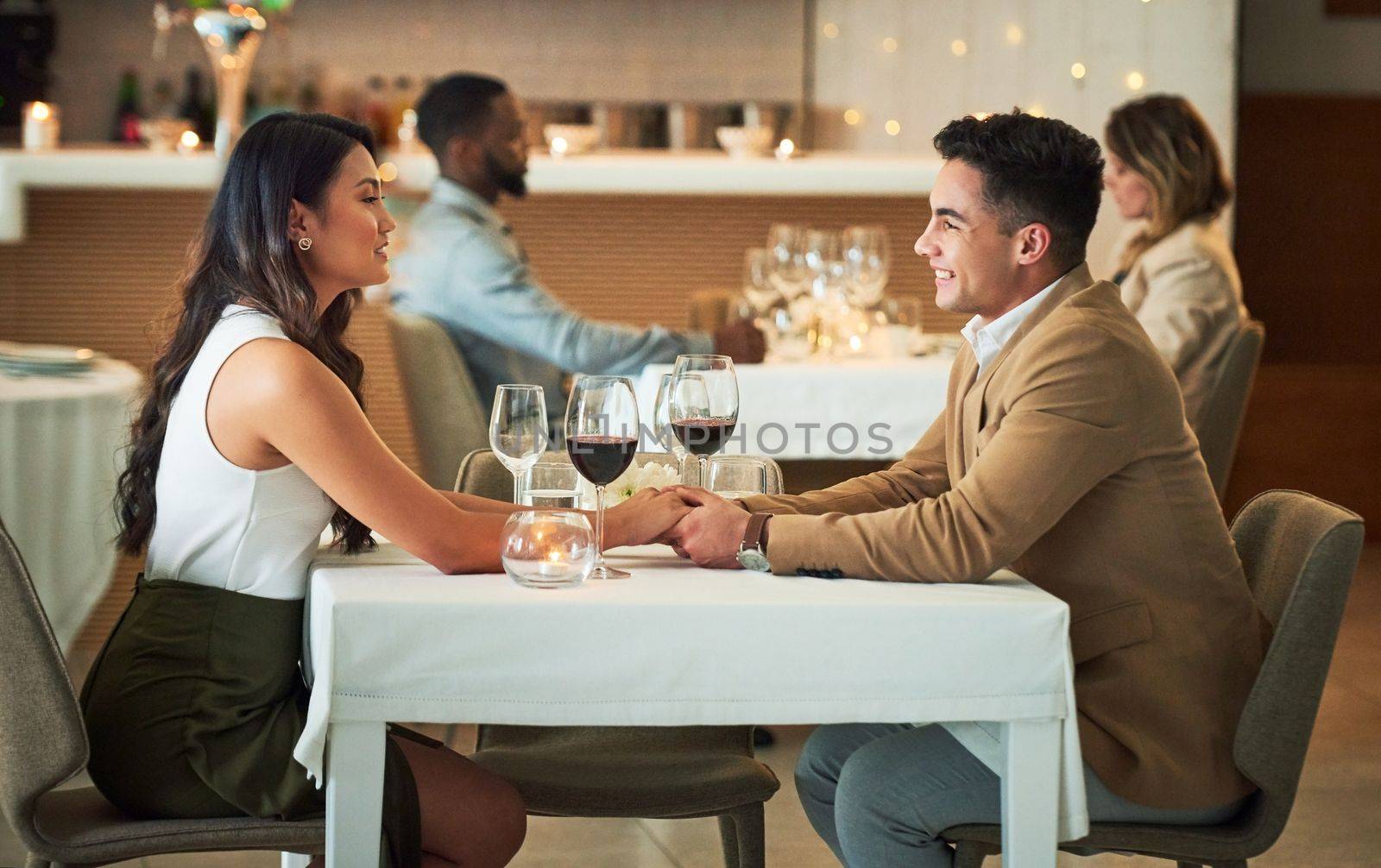 Couple in restaurant for dinner, holding hands and romantic date on Valentines day, love and celebrate holiday. Commitment, interracial relationship and man with woman, trust, support and celebration.