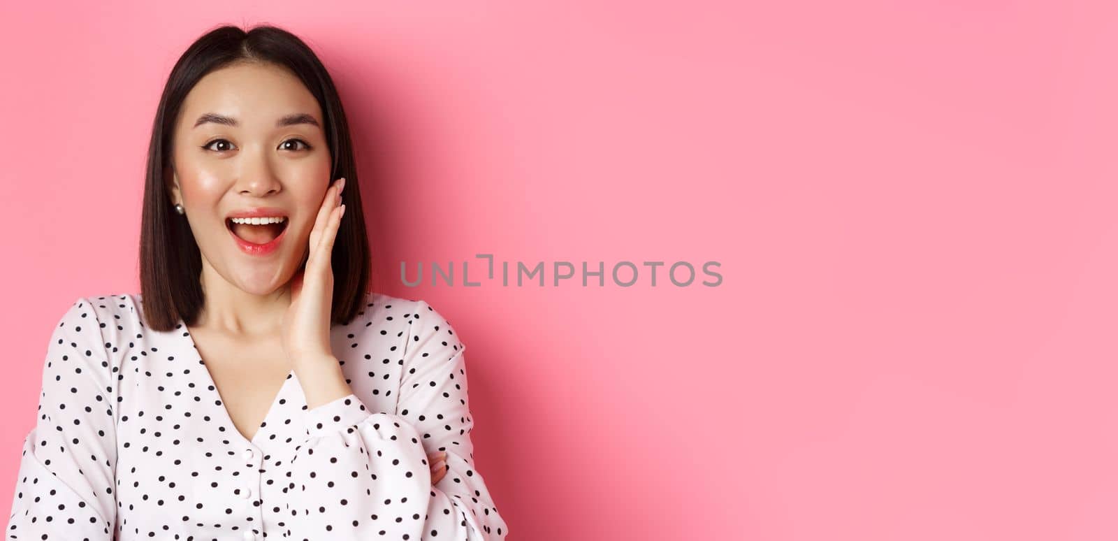 Close-up of beautiful asian woman calling for you, making announcement or yelling, standing over pink background.