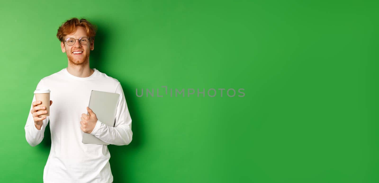 Handsome young man, employee with laptop drinking coffee on break, smiling satisfied, standing over green background by Benzoix