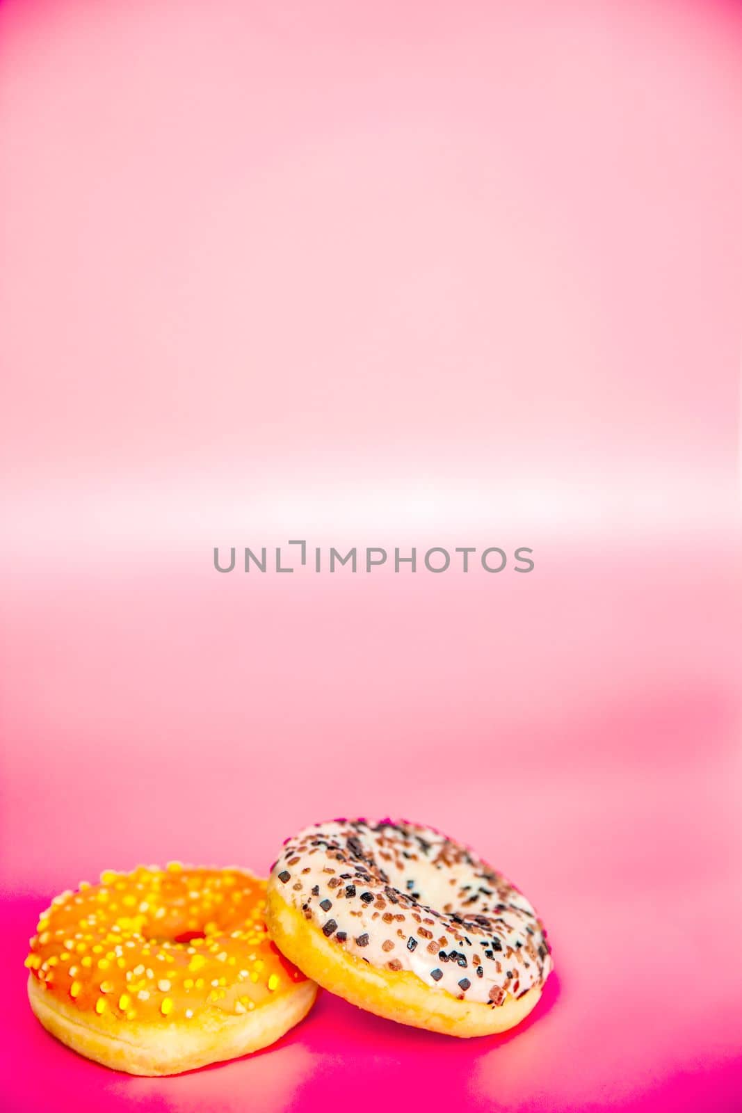Sweet donuts stacked in a stack on a pink background. Copy space, various glaze and sprinkels chocolate chip, snack fast food sweets concept candy