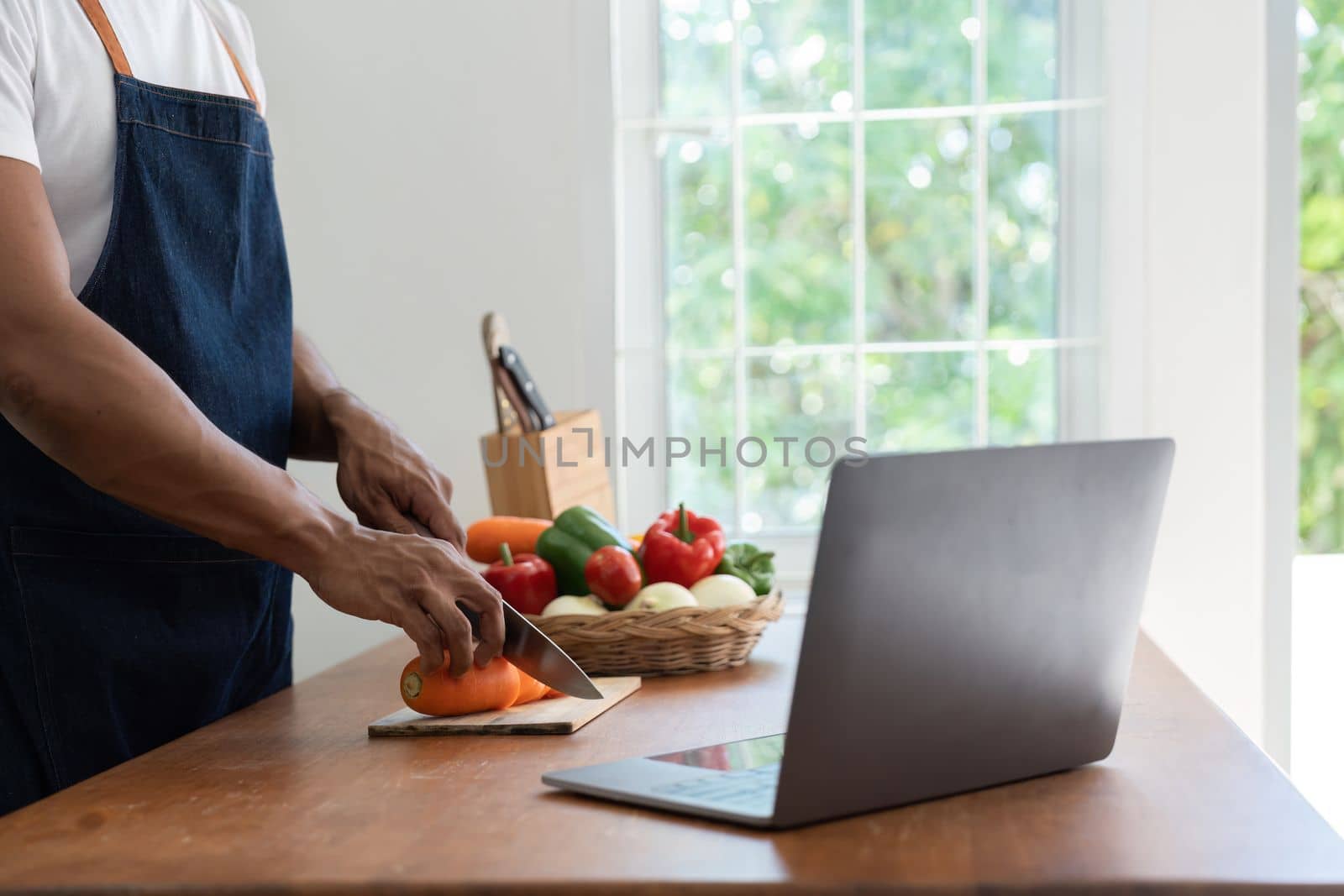 Man in kitchen looking at recipes on laptop while cooking.