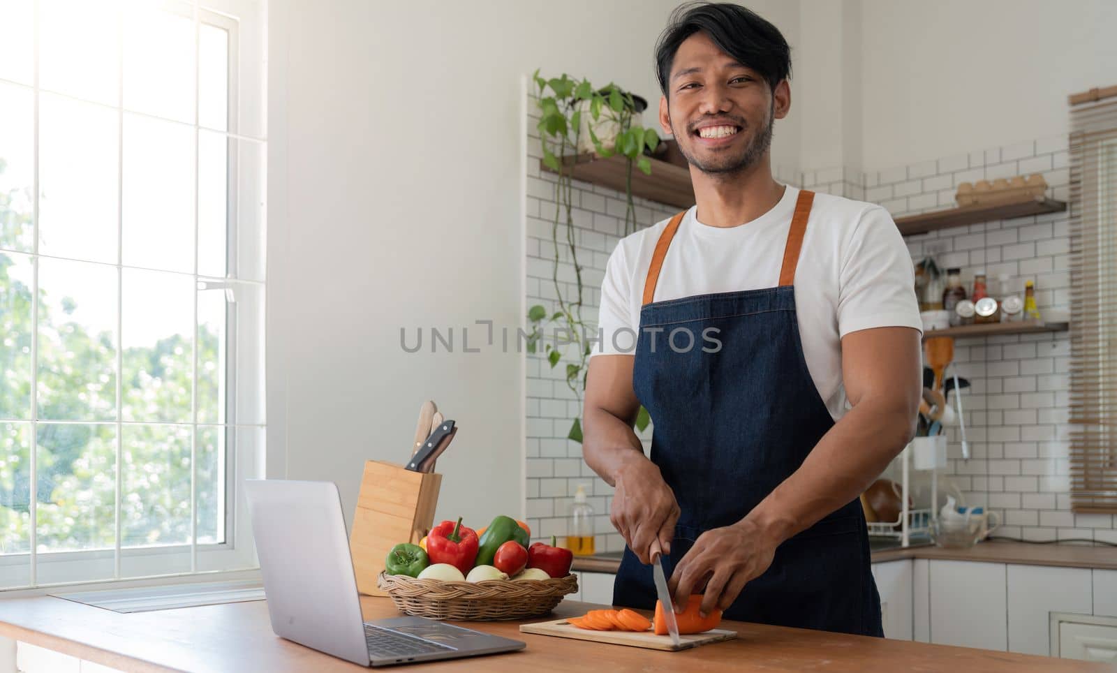 Man in kitchen looking at recipes on laptop while cooking.