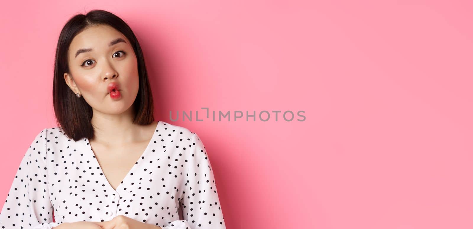 Beauty and lifestyle concept. Close-up of funny and cute asian woman pucker lips, showing fish mouth and standing playful, standing over pink background.