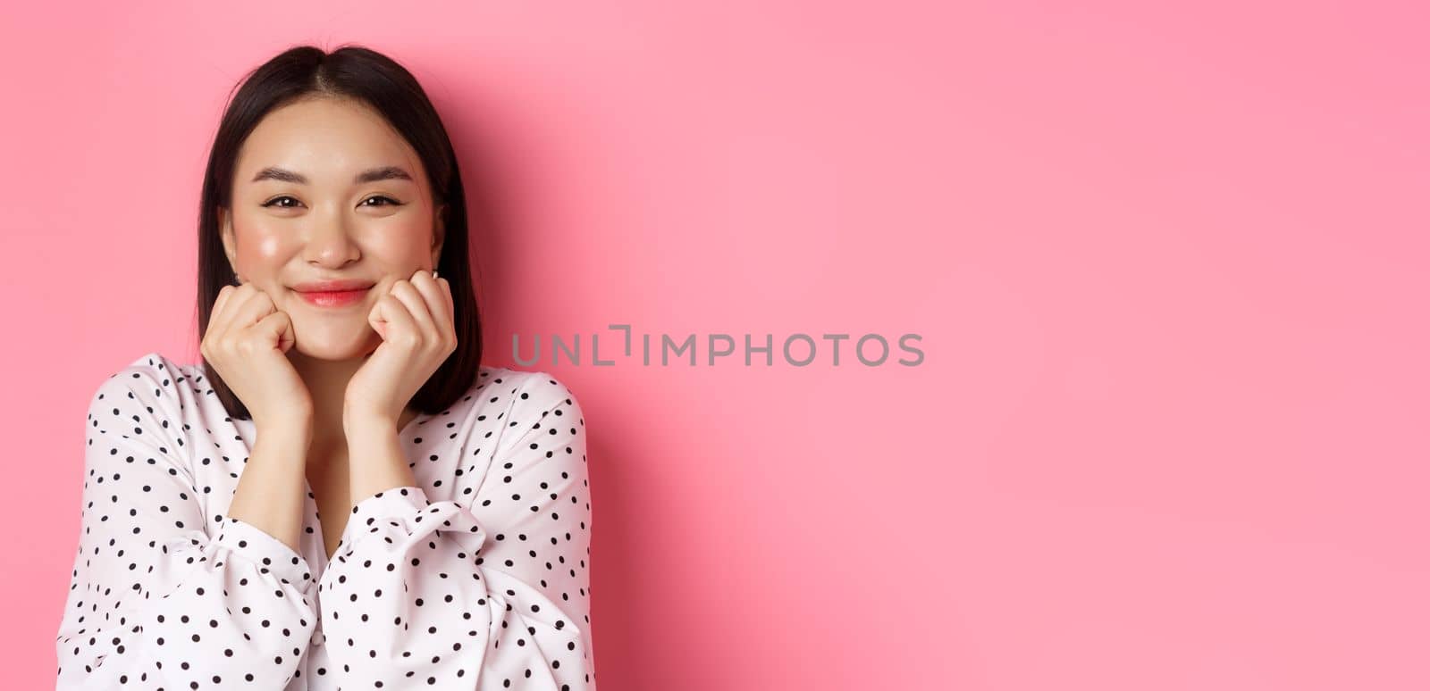 Beauty and lifestyle concept. Close-up of adorable asian woman showing puffy cheeks, smiling and looking happy, standing over pink background.