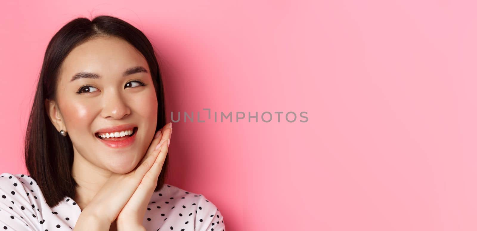 Beauty and skin care concept. Headshot of adorable and dreamy asian woman looking left, smiling and imaging, standing against pink background by Benzoix